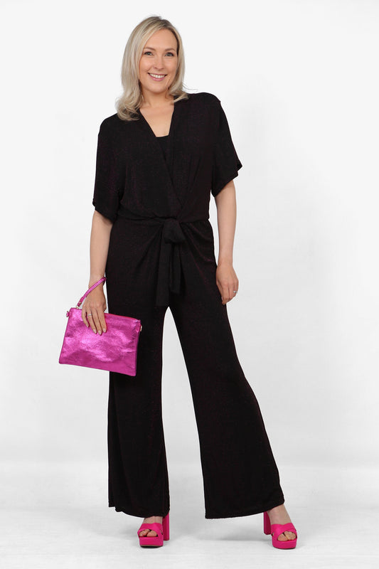 Model wearing black and fuchsia glitter deep V-neck jumpsuit with deep V-neck. Holding fuchisa metallic clutch bag. Glittery night out outfit