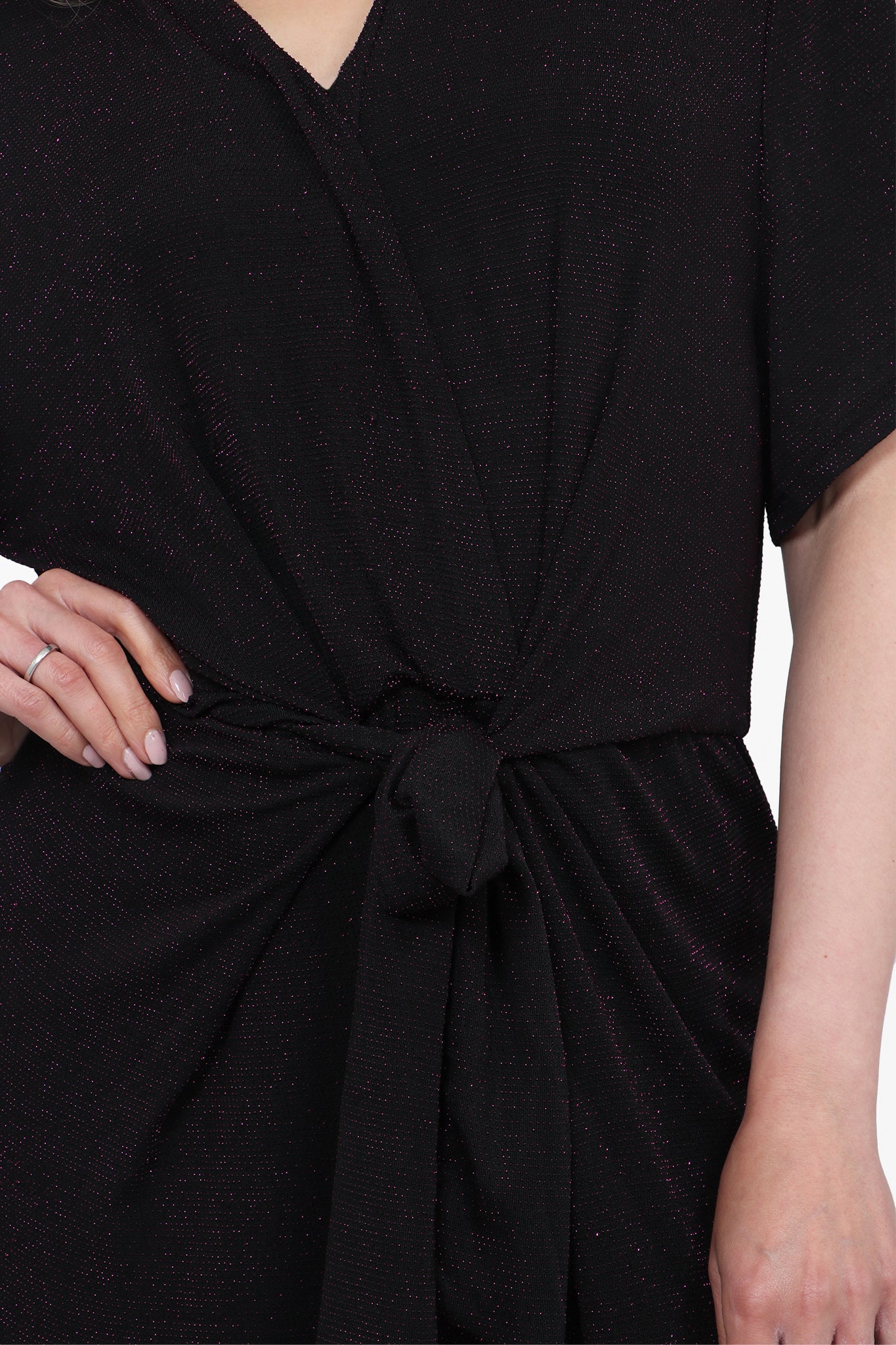 Close up of model wearing fuchsia and black glittery deep V-neck jumpsuit. Tie detail shown